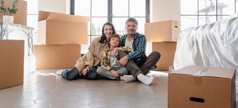 Family sitting on the floor among moving boxes in a bright living room with a dog in front