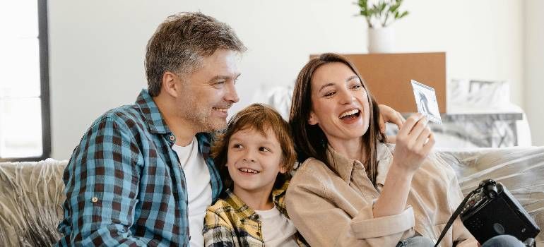 Three people smiling on a couch, taking a selfie in a bright living room