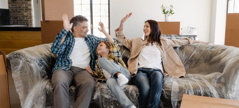 Three people on a couch in a bright living room, smiling and raising their hands together