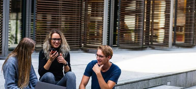 Three people talking and sitting on steps outside a modern building