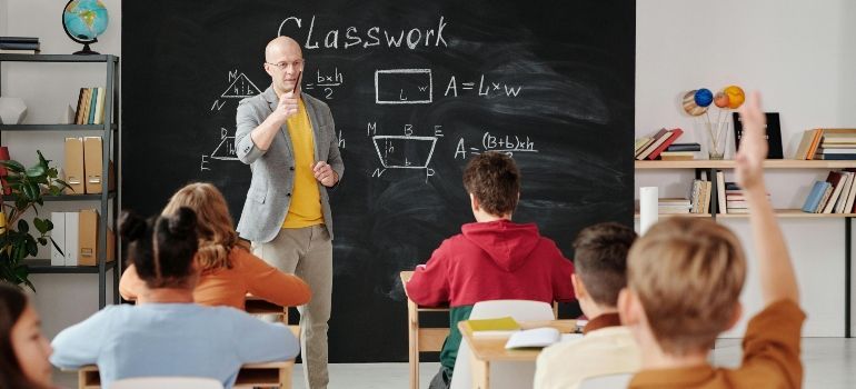 Teacher at a blackboard teaching a classroom of students with raised hands