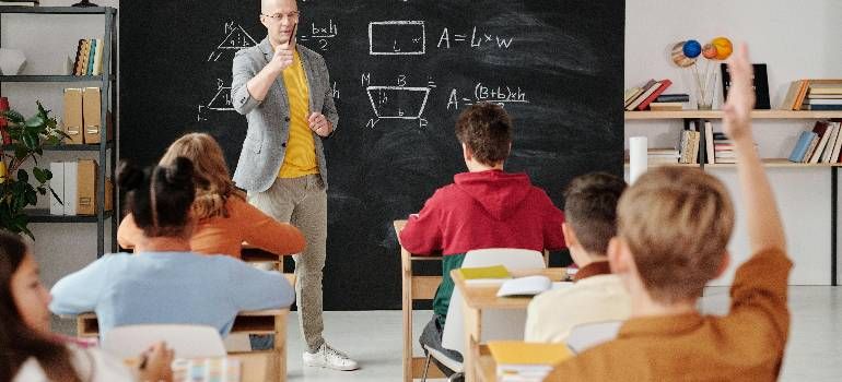 Teacher pointing at chalkboard while students sit at desks in a classroom