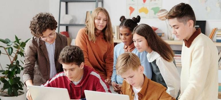 Group of students gathered around a laptop in a classroom, collaborating and smiling
