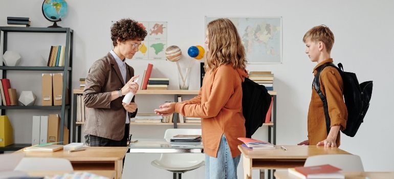 Students chatting in a classroom with desks, backpacks, and a globe on a shelf