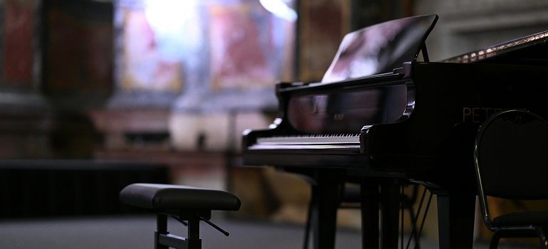 A black grand piano and bench in a dimly lit room with blurred background.