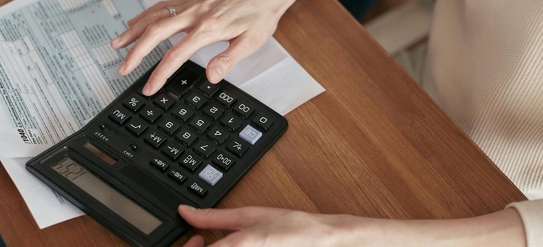 Hands using a black calculator on a wooden desk beside papers and a notebook