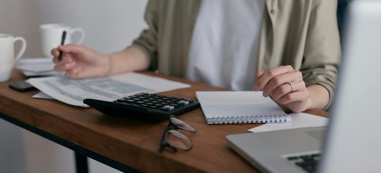 Person working at a desk with calculator, notebook, and laptop