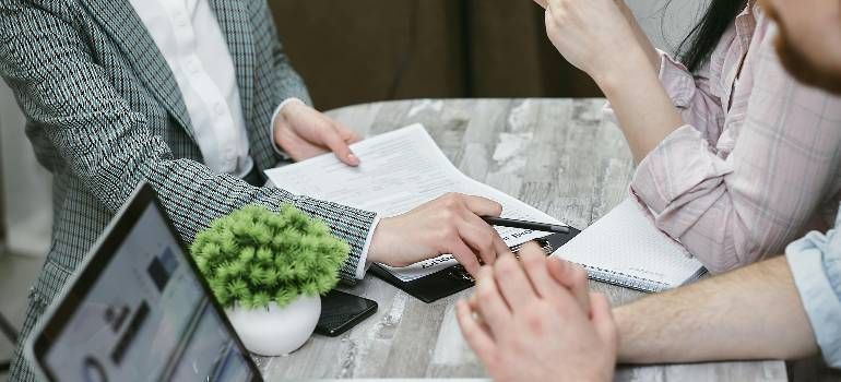 Business meeting with three people discussing documents around a laptop on a desk