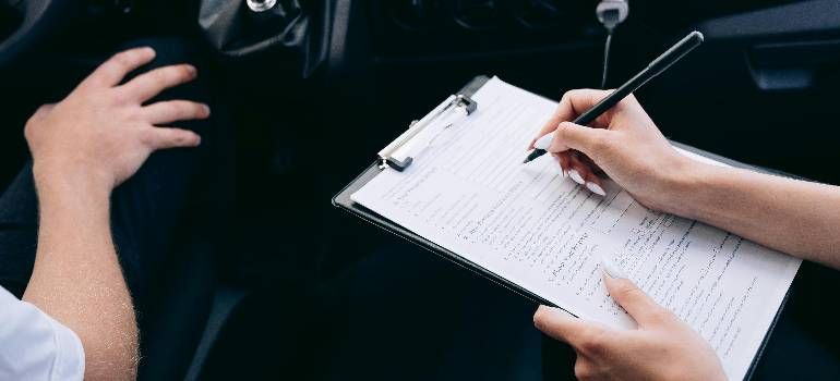 Hands writing on a clipboard beside a person in a car interior