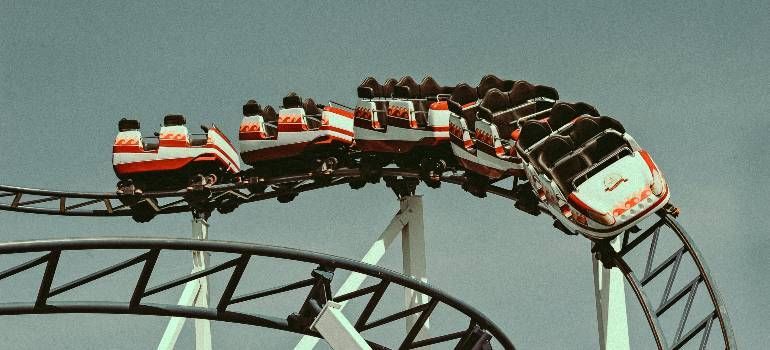 Roller coaster train cresting a steep drop on a black track, with riders leaning forward