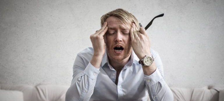 Stressed person in a white shirt holding their head on a couch, looking overwhelmed.