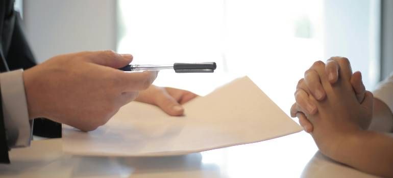 Hands exchanging a document across a table, with one person holding a pen.