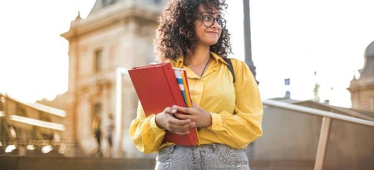 Person in a yellow shirt holding a red notebook outdoors near a stone building