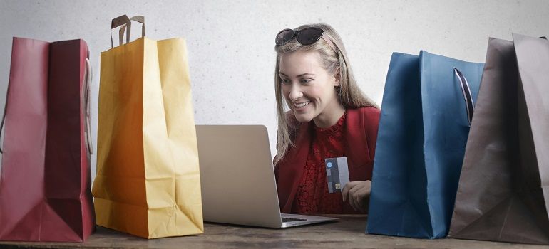 Woman smiling at a laptop, surrounded by colorful shopping bags on both sides