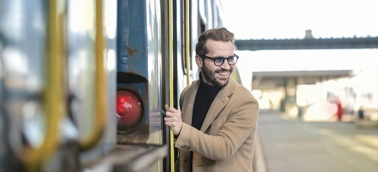 Man in a tan coat smiling while boarding a train at a station platform