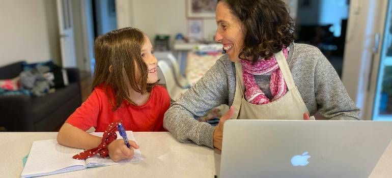 Woman and child smiling at each other across a table, with a laptop and papers in a bright room
