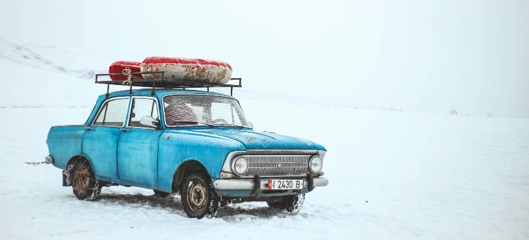 Blue vintage car with roof luggage driving through snow in a white, wintry landscape