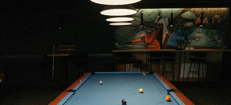 Pool table in a dim bar, with scattered balls and hanging lights overhead.
