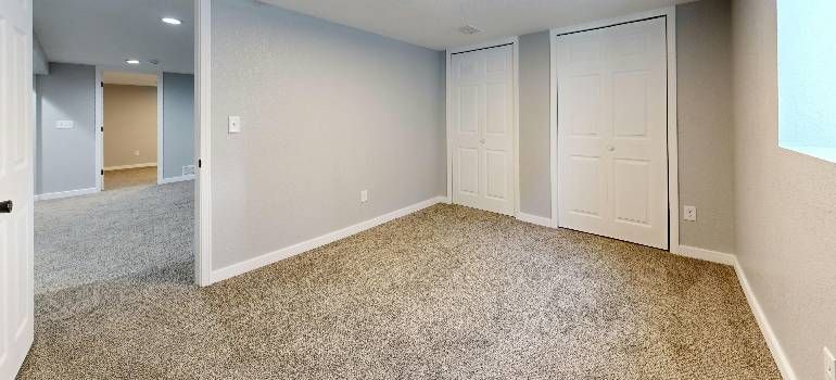 Empty beige bedroom with carpet, double closet doors, and a partial view into a bathroom