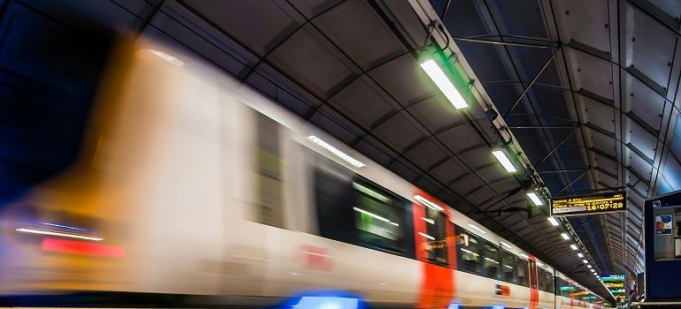 Blurred train speeding through a covered station platform at night, with bright lights overhead