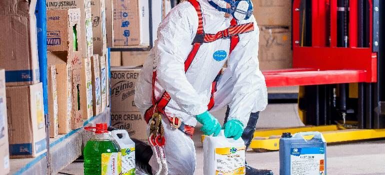 Worker in white hazmat suit handling containers in a warehouse aisle