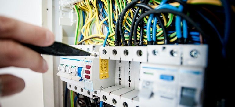 Technician wiring an electrical breaker panel with blue, yellow, and green cables.