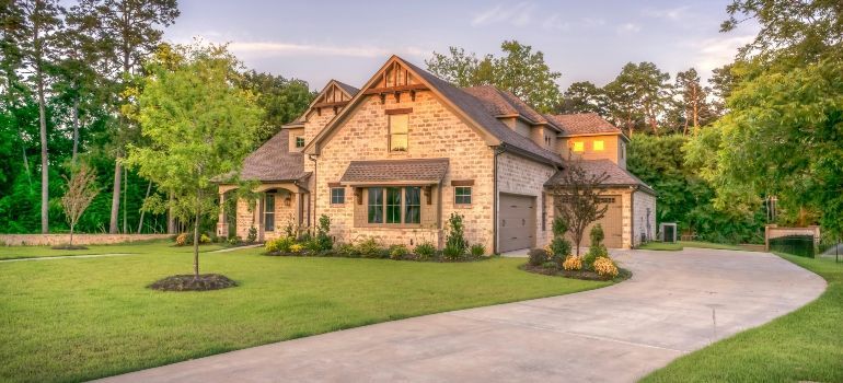 Large stone house with a peaked roof, manicured lawn, and a curved driveway at sunset
