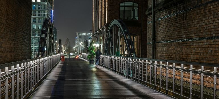 Nighttime wet pedestrian bridge with railings and city lights reflecting on the walkway