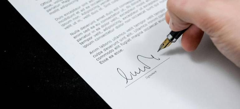 Hand signing a document with a black pen on a white page