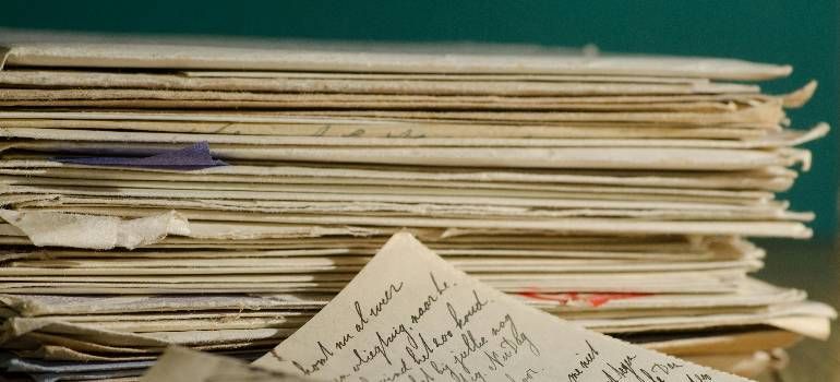 Stack of papers with handwritten notes, viewed from the side on a table, with a teal background