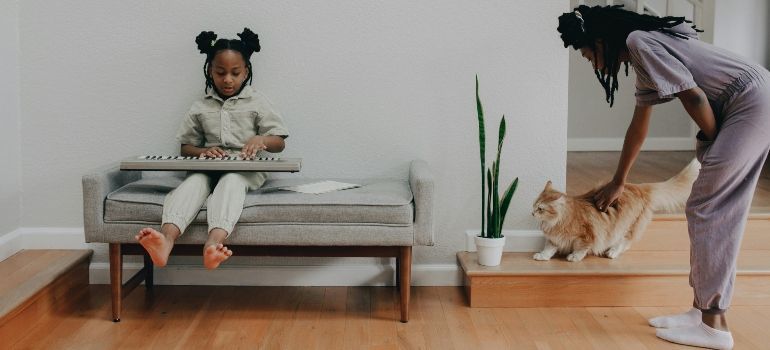 Child sitting on a couch while a person pets a dog beside a potted plant