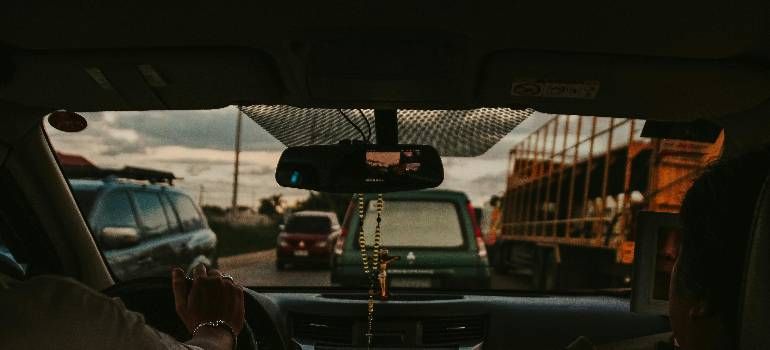 View from inside a car in heavy traffic, with a green van ahead and trucks along a road at sunset.