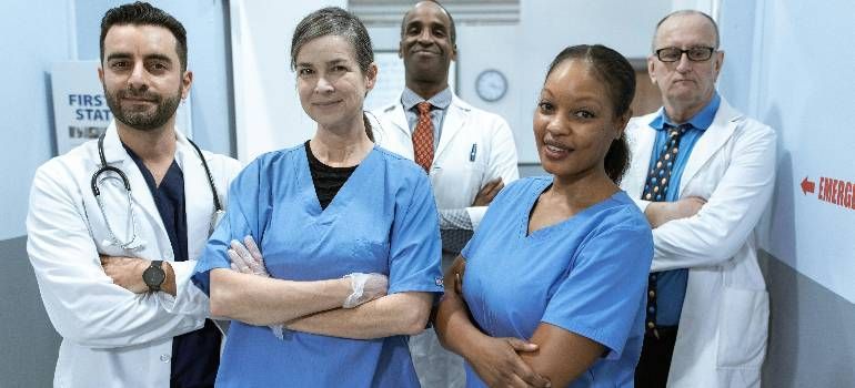 Healthcare team in blue scrubs and white coats standing together in a clinic hallway