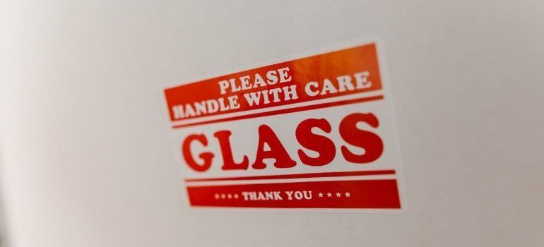 Red glass warning label reading “Please handle with care” and “Glass” on a white surface