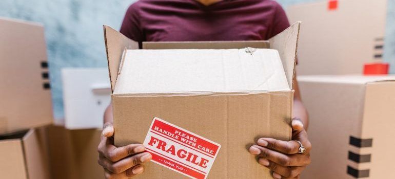 Person holding an open cardboard box labeled “FRAGILE” in a warehouse