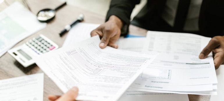 Hands reviewing paperwork at a desk with a calculator and magnifying glass