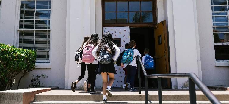 Students entering a building through open doors, carrying backpacks and stepping up the entrance stairs
