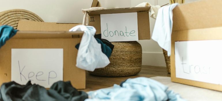 Cardboard donation boxes labeled keep, donate, and toss, with folded clothes scattered around them