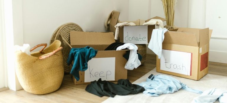 Cardboard moving boxes and a woven basket filled with clothes on a sunlit floor