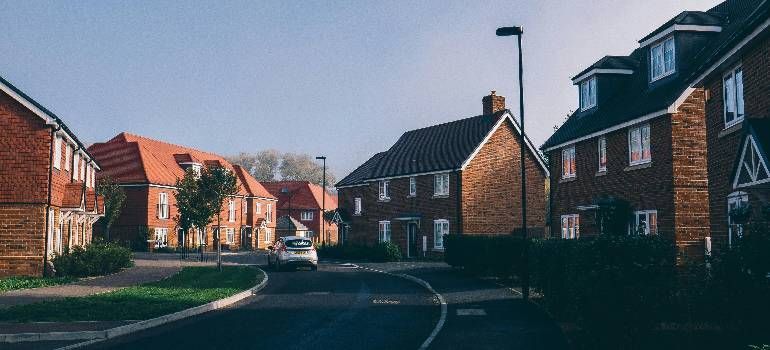Quiet suburban street with red-brick houses, parked cars, and a clear blue sky