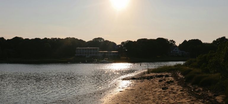Sunlit lake shoreline with rippling water, sandy beach, and trees silhouetted against the sky