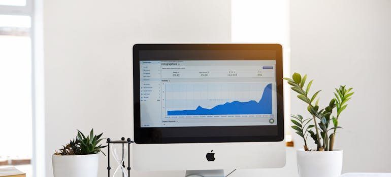 IMac displaying a blue analytics chart on a white desk with small potted plants