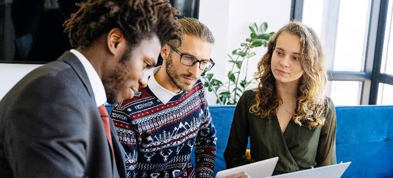 Three coworkers review documents in a bright office, discussing papers together.