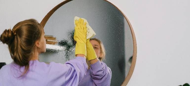 Person in purple cleaning a round mirror with a yellow cloth in a home interior