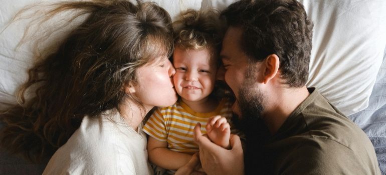 Parents kissing a smiling child between them on a bed
