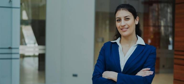 Woman in a blue blazer standing with arms crossed in a modern office setting