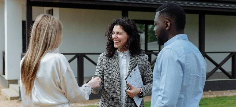 Three people talking and shaking hands outside a building.