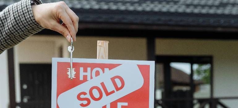 Hand placing a red SOLD sign on a home for sale sign outdoors