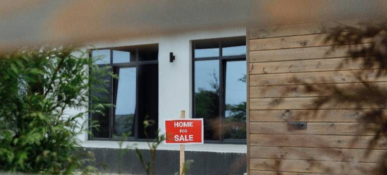Modern house exterior with windows and a red “Home for Sale” sign by the front door
