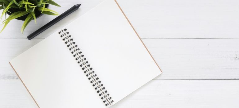 Blank spiral notebook on a white desk with a green plant and black pen in the corner